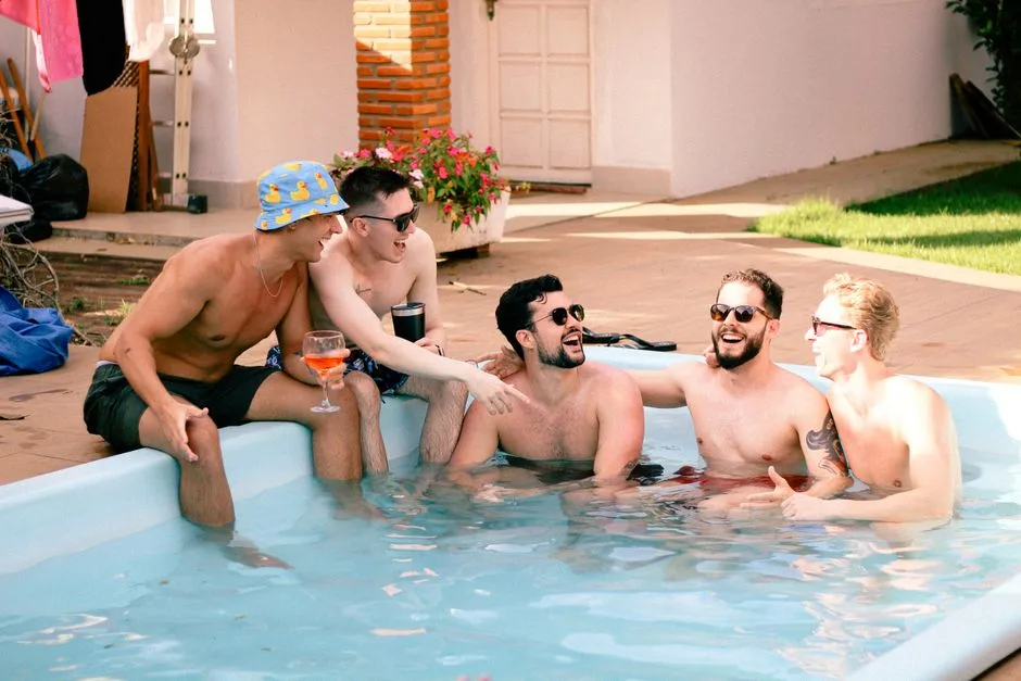 A group of men having fun and relaxing in a backyard pool under the sun.
