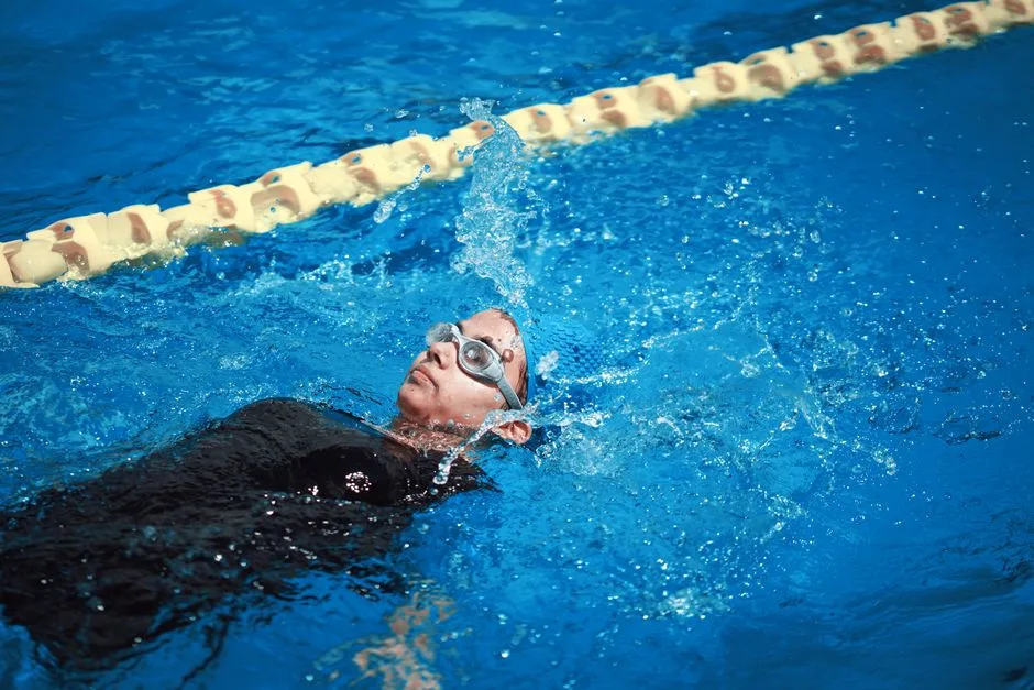 A female swimmer doing a backstroke in a clear blue swimming pool. Perfect for sports and lifestyle themes.